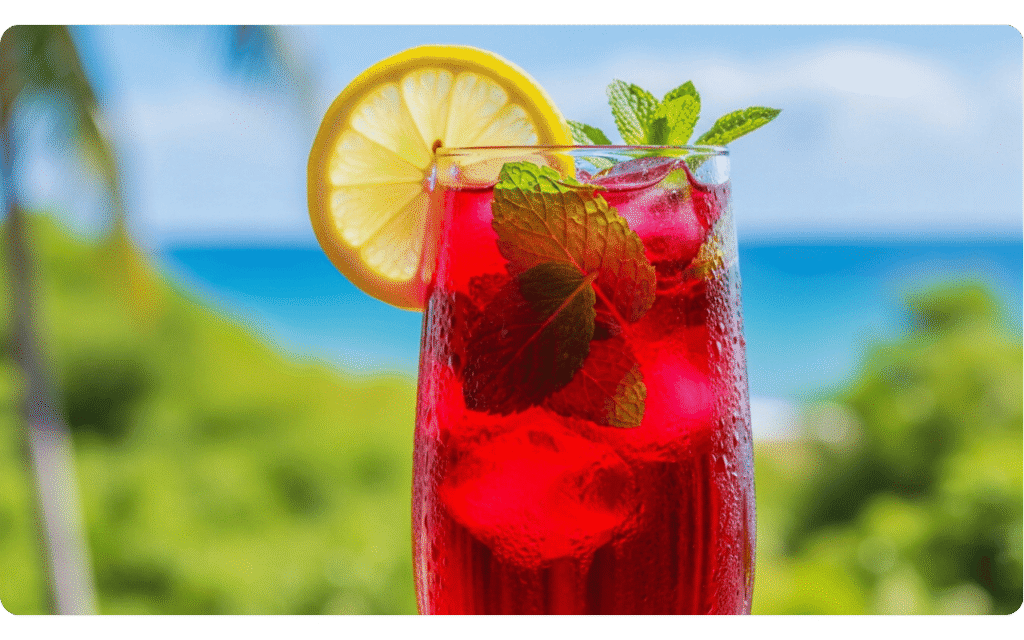 Bebida vermelha com limão e folhas de hortelã em fundo tropical.