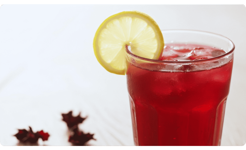 Copo de chá gelado vermelho com fatia de limão sobre mesa branca.