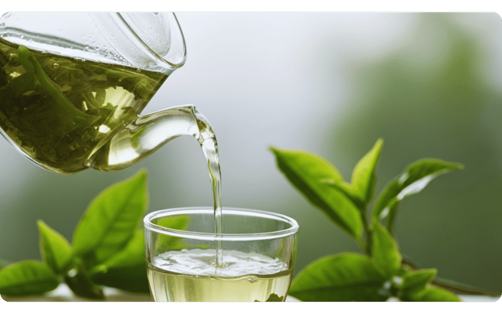Bule de vidro vertendo chá verde quente em um copo transparente.