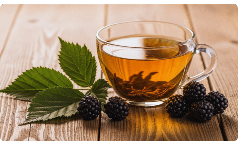 Xícara de chá com folhas de amora e amoras sobre mesa de madeira.