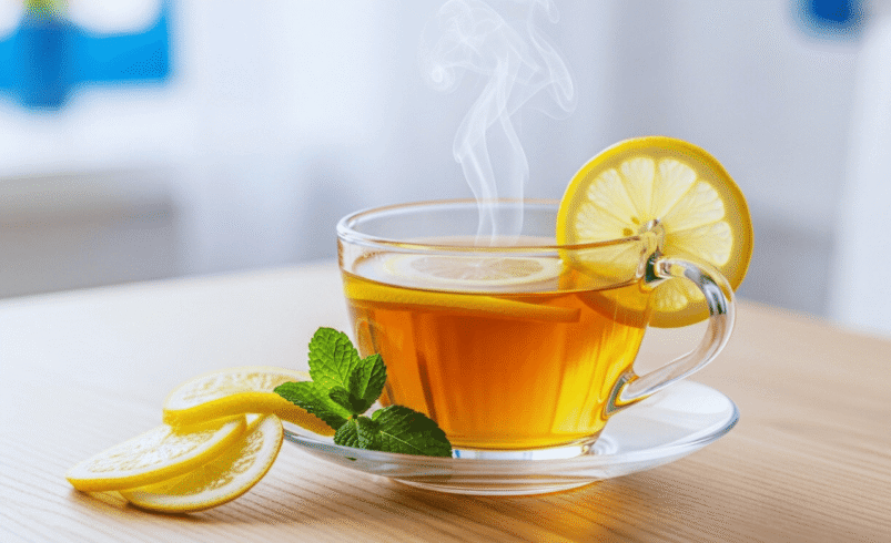 Xícara de chá quente com limão e hortelã sobre mesa de madeira.