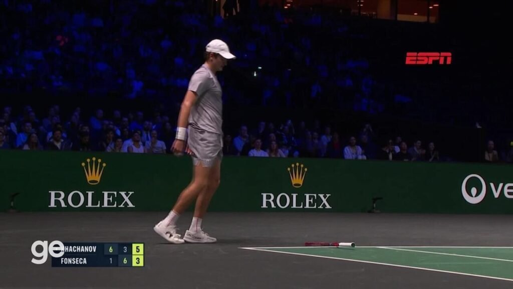 Quadra de tênis, jogador em ação e placar exibido ao fundo.