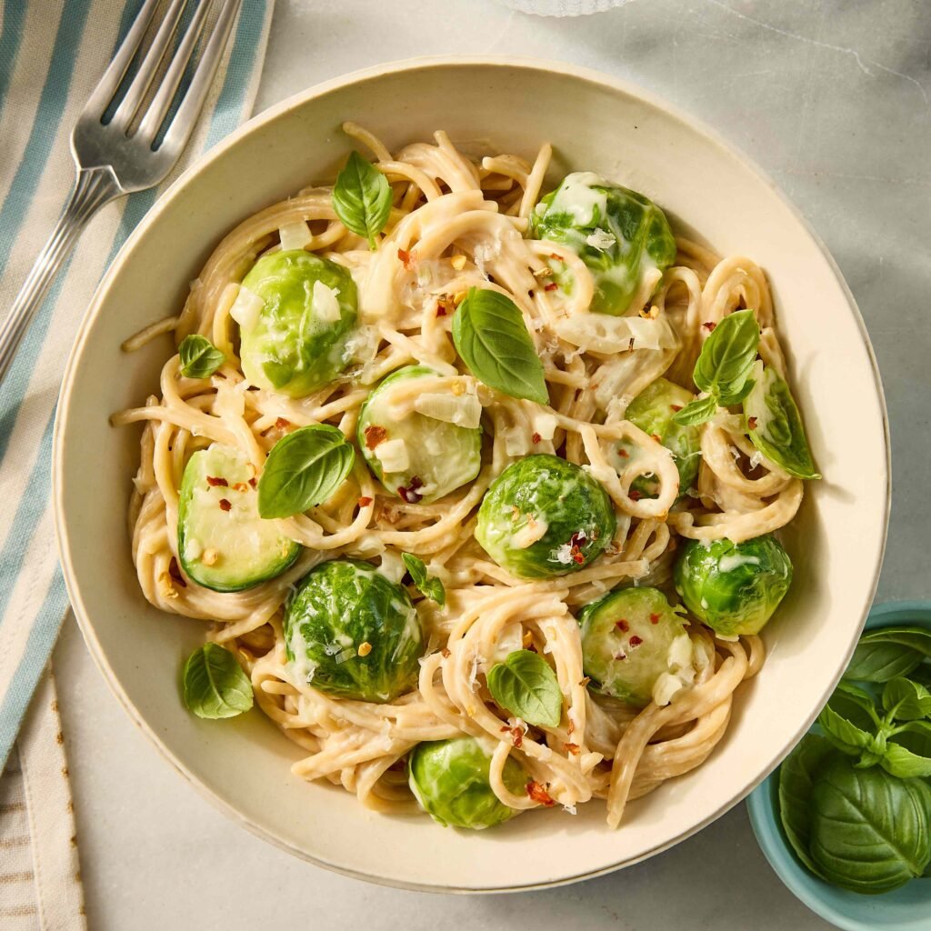 Prato de macarrão com molho cremoso, couve de bruxelas e manjericão.