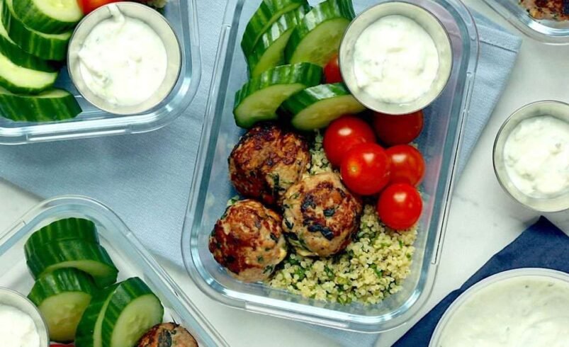 Marmitas com almôndegas, vegetais frescos e molho de iogurte ao lado.