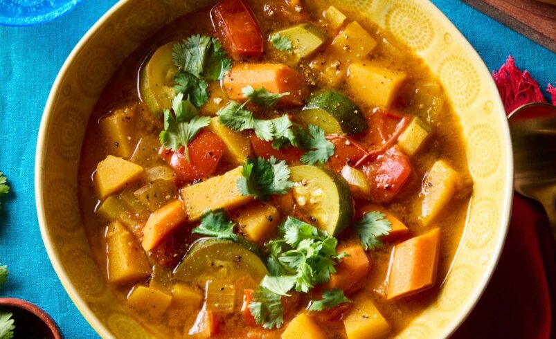 Tigela amarela com ensopado de legumes variados, decorado com coentro.