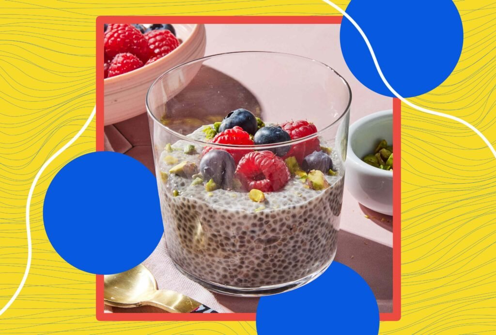 Tigela de chia decorada com frutas vermelhas e pistache em fundo colorido.