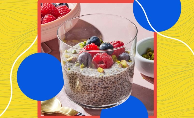 Tigela de chia decorada com frutas vermelhas e pistache em fundo colorido.