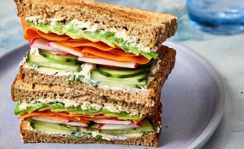 Sanduíche com vegetais frescos, pão integral e creme servido em prato azul.
