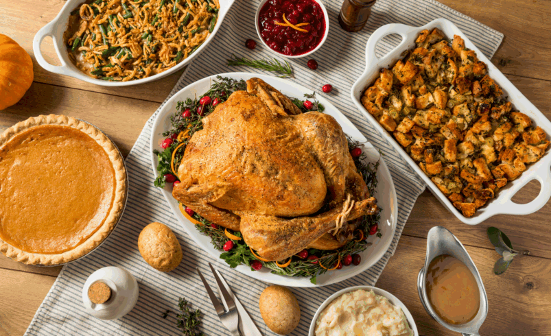 Mesa com peru assado, torta de abóbora, purê, molho e outros pratos típicos.