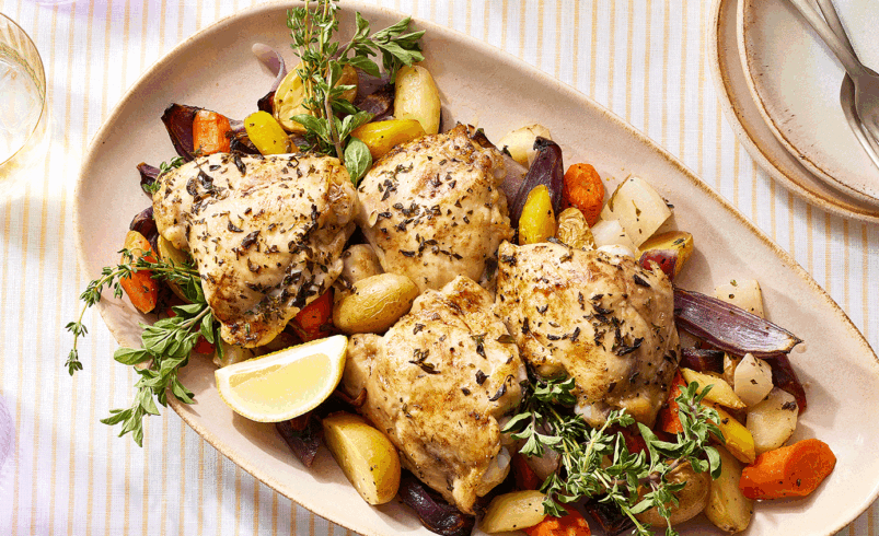 Prato oval com pedaços de frango assado, legumes e ervas frescas.