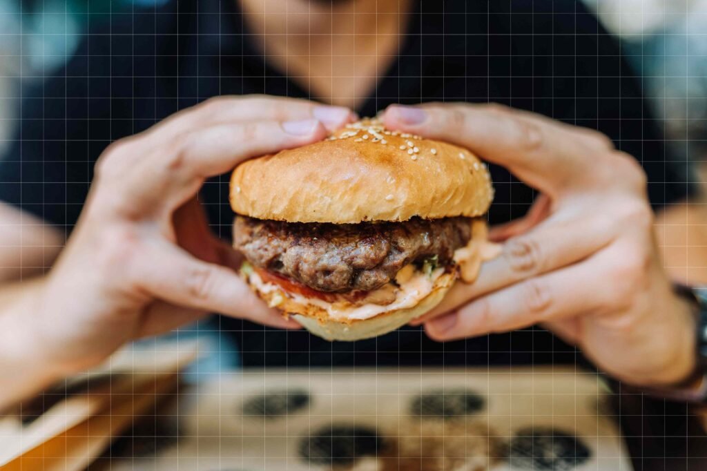 Pessoa segurando um hambúrguer artesanal com carne suculenta e molho.