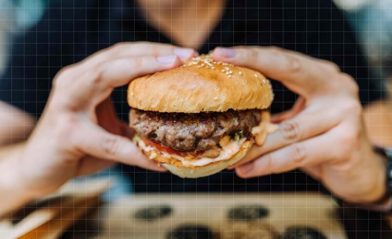 Pessoa segurando um hambúrguer artesanal com carne suculenta e molho.