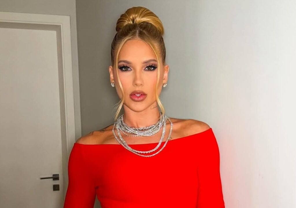 Figura feminina com vestido vermelho ombro a ombro e colares brilhantes.