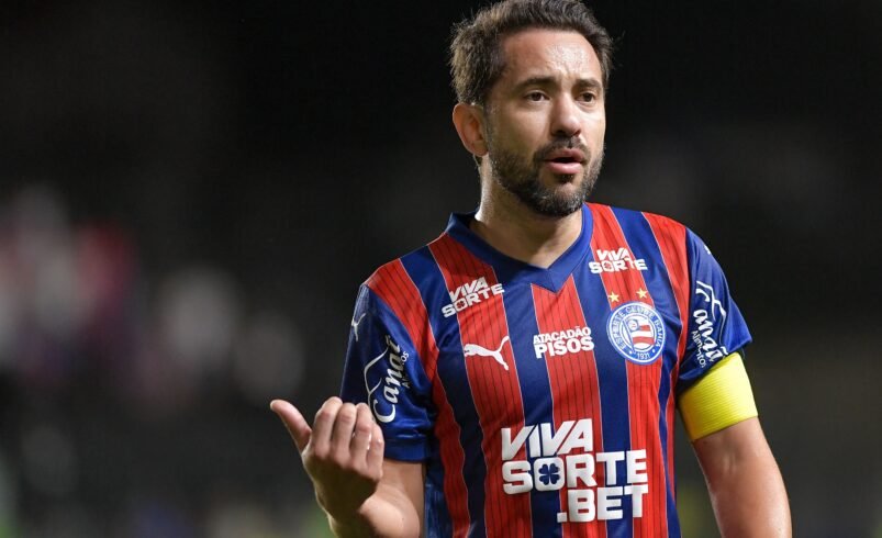 Jogador de futebol com uniforme vermelho e azul e braçadeira de capitão.
