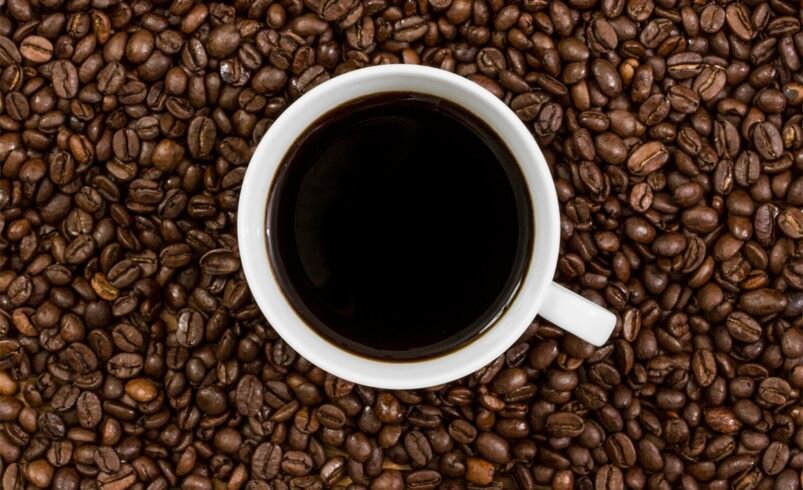 Xícara de café preto cercada por grãos de café torrados.