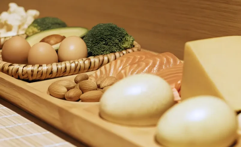 Bandeja de madeira com salmão, ovos, queijo, nozes, abacate, brócolis e cogumelos.