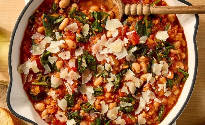 Panela com ensopado de feijão, espinafre, tomate e lascas de queijo.