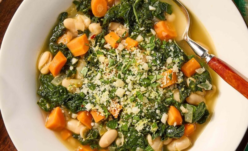 Prato com sopa de vegetais, feijão branco e parmesão ralado em destaque.