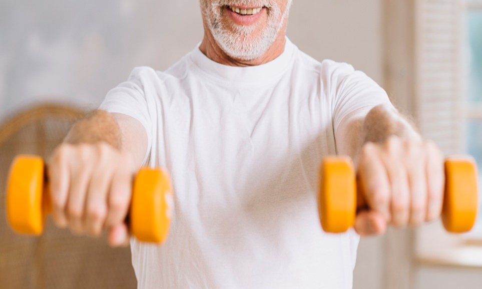 Homem idoso segurando halteres laranja durante exercício físico.
