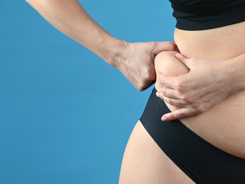 Mulher segurando a lateral do abdômen com as mãos, fundo azul.