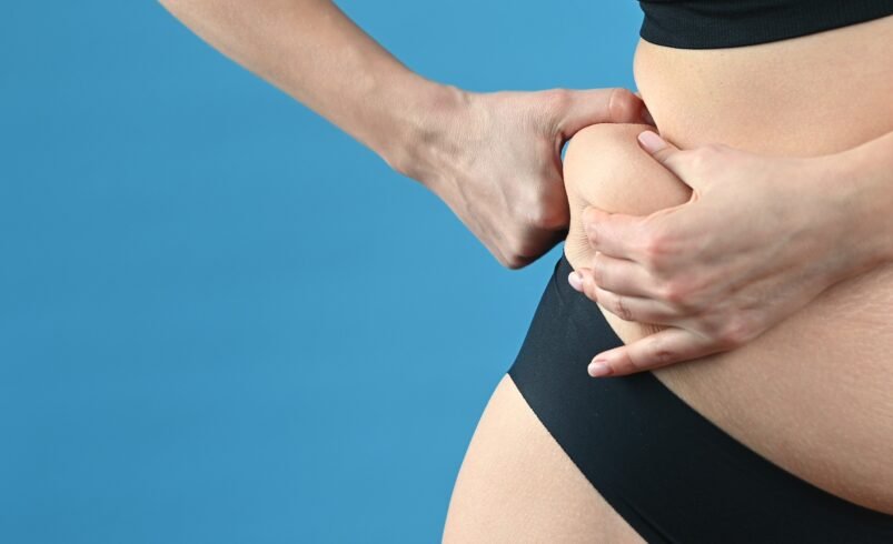 Mulher segurando a lateral do abdômen com as mãos, fundo azul.