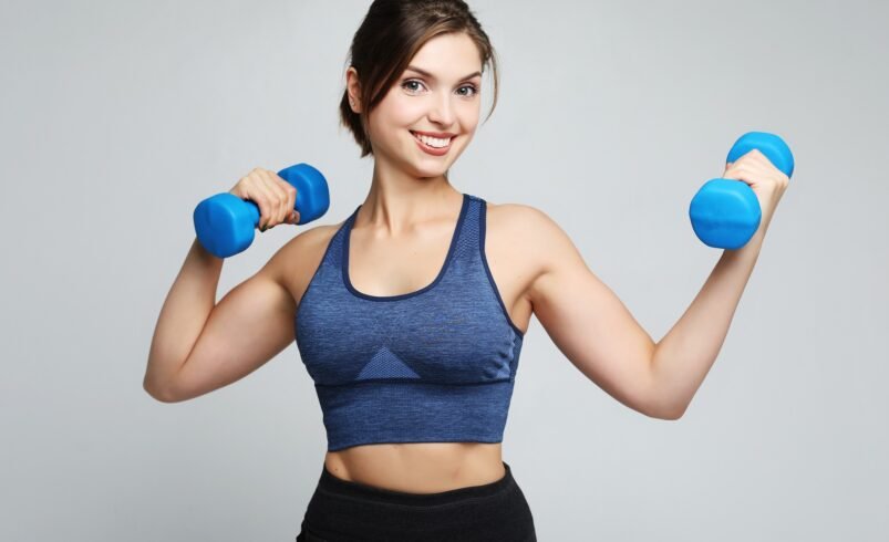 Mulher segurando dois halteres azuis em movimento de flexão de braços.