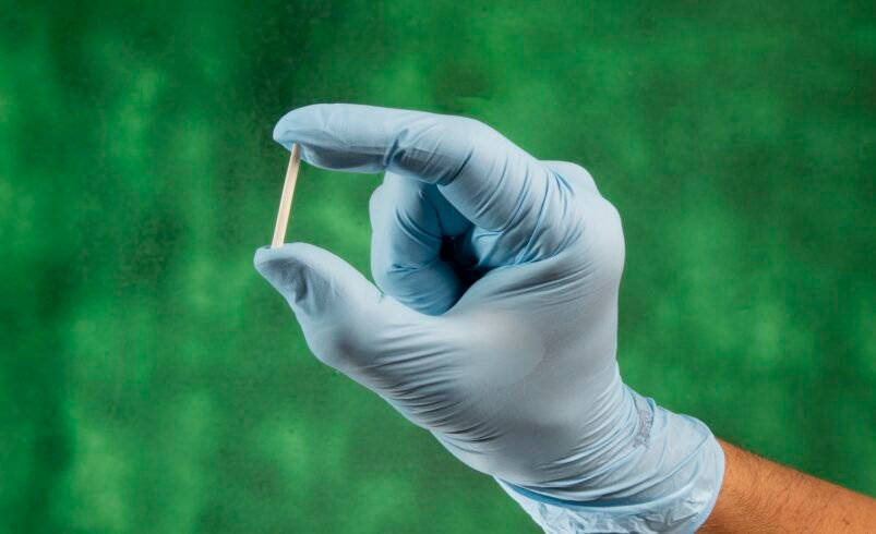 Mão enluvada segurando um pequeno objeto com fundo verde.