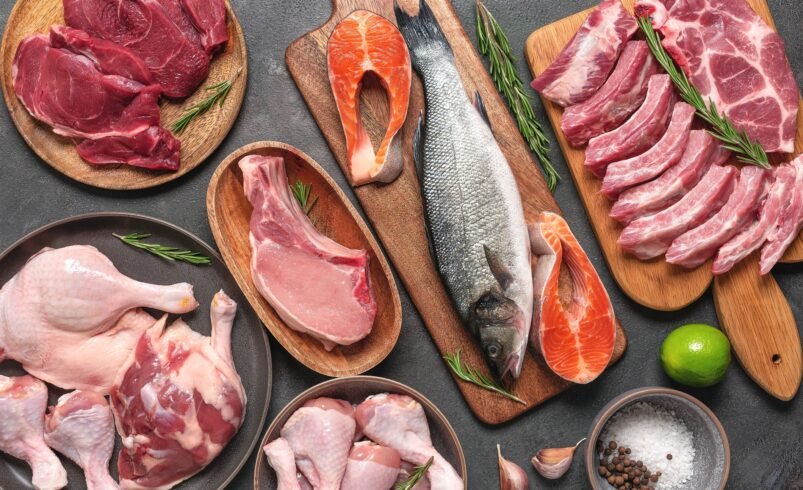 Diversos tipos de carnes como peixe, frango e carne bovina dispostos em pratos e tábuas.