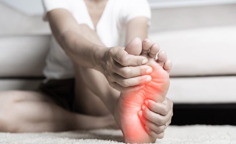 Pessoa segurando a sola do pé com área em destaque vermelho indicando dor.