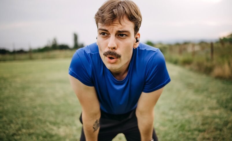 Pessoa em camiseta azul descansando em área verde aberta após exercício.