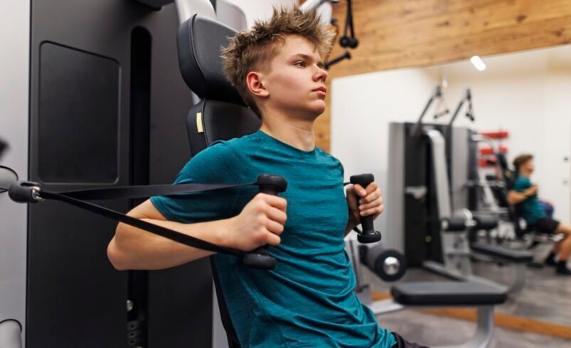 Pessoa em camiseta azul utilizando máquina de musculação em academia.