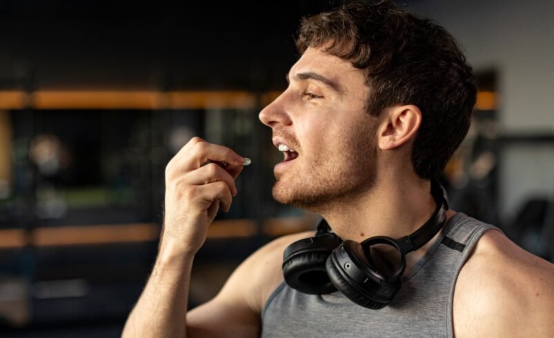 Homem usando regata e fones de ouvido no pescoço em uma academia.