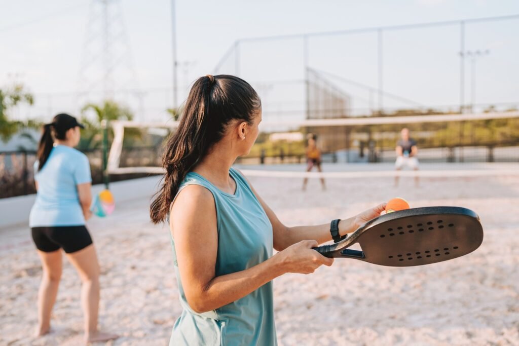Pessoa segurando raquete de beach tennis em quadra de areia.