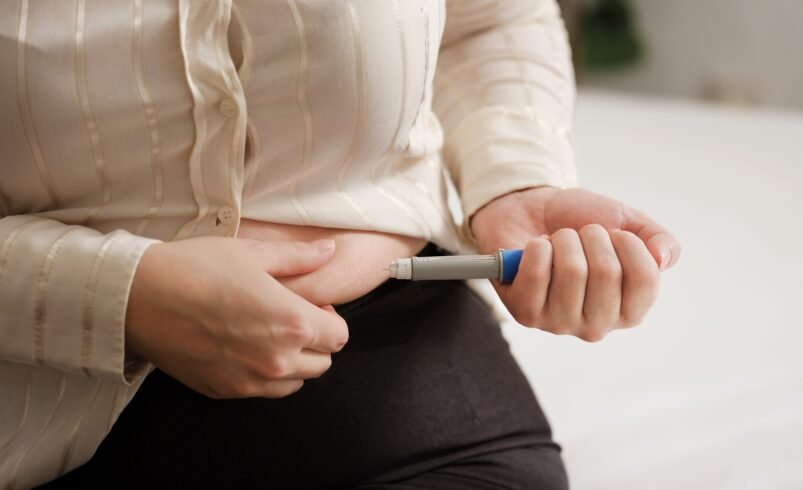 Pessoa aplicando injeção subcutânea no abdômen com caneta injetora.