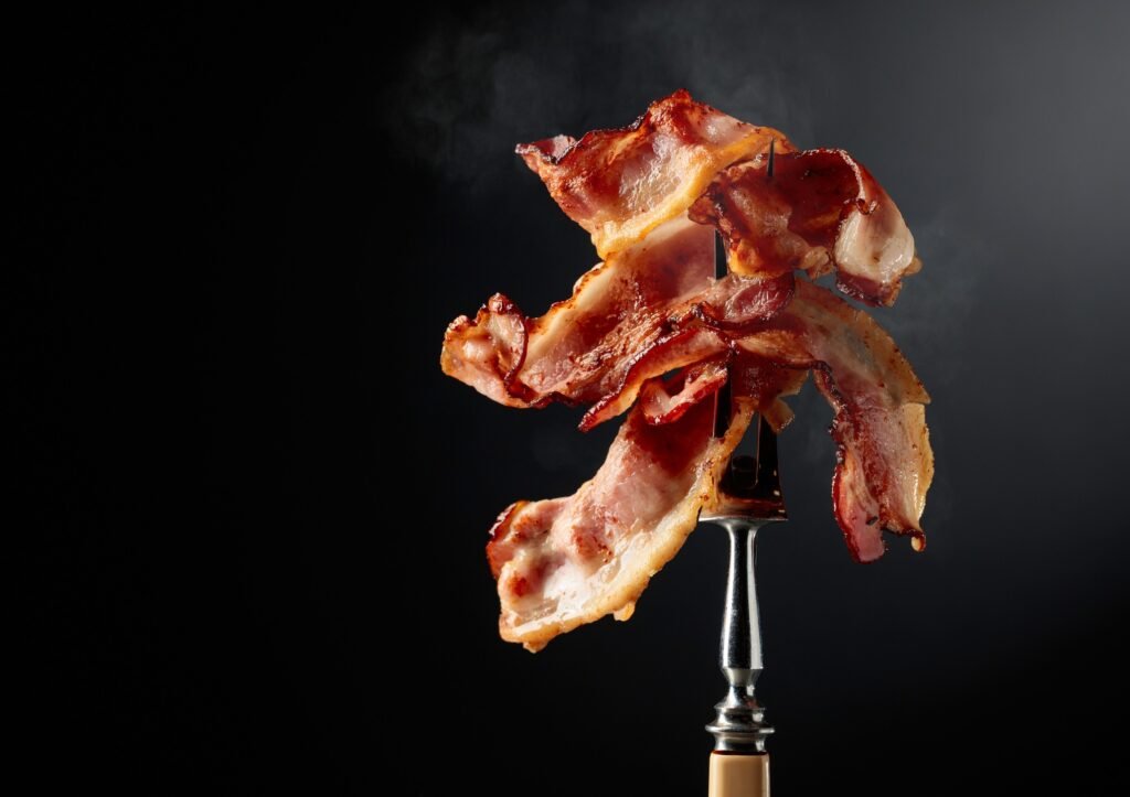 Fatias crocantes de bacon empilhadas em um garfo, com fundo escuro.