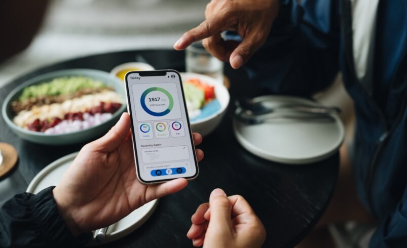 Pessoa segurando celular com app de saúde, ao lado de refeições saudáveis.