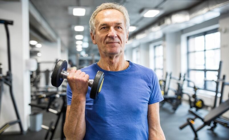Pessoa segurando halter em academia com equipamentos ao fundo.