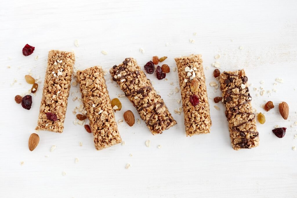 Cinco barras de granola decoradas com chocolate, frutas secas e castanhas.