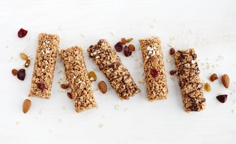 Cinco barras de granola decoradas com chocolate, frutas secas e castanhas.