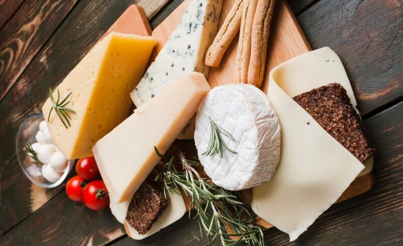 Mesa com queijos variados, tomatinhos, grissinis e alecrim.