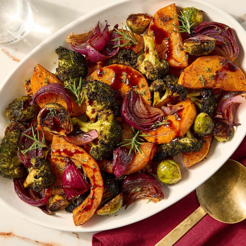Prato de legumes assados, incluindo batata-doce, brócolis, cebola roxa e couve de Bruxelas.