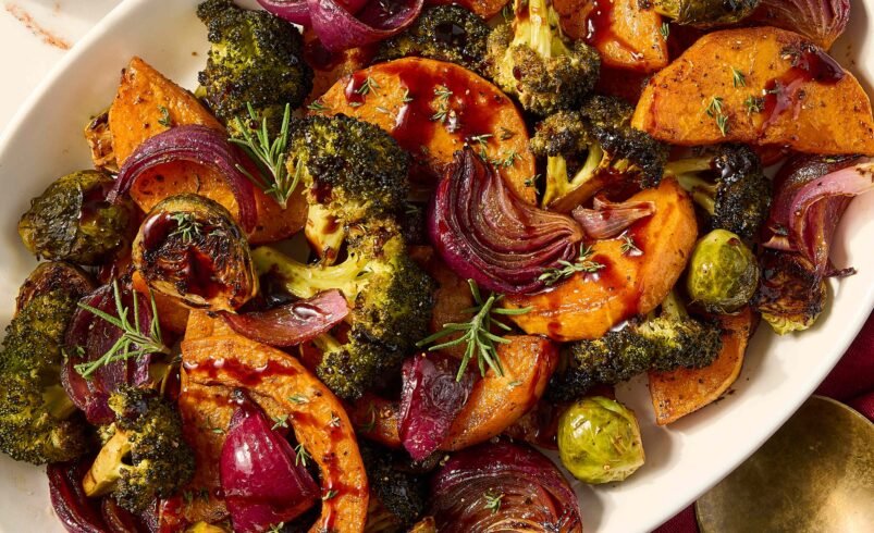 Prato de legumes assados, incluindo batata-doce, brócolis, cebola roxa e couve de Bruxelas.
