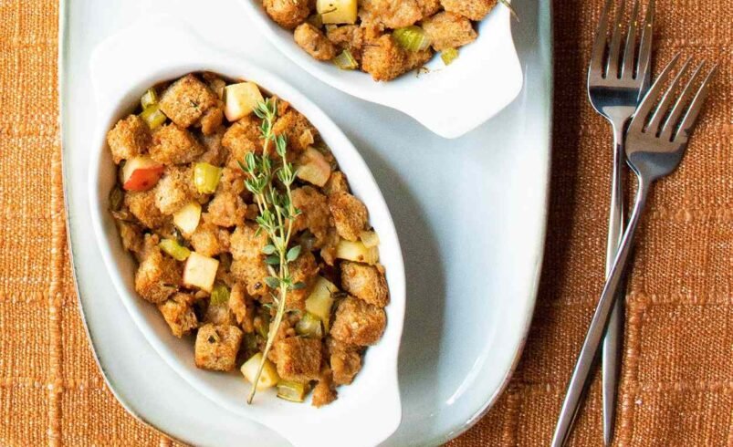 Dois pratos brancos com stuffing, decorados com tomilho sobre uma toalha laranja.