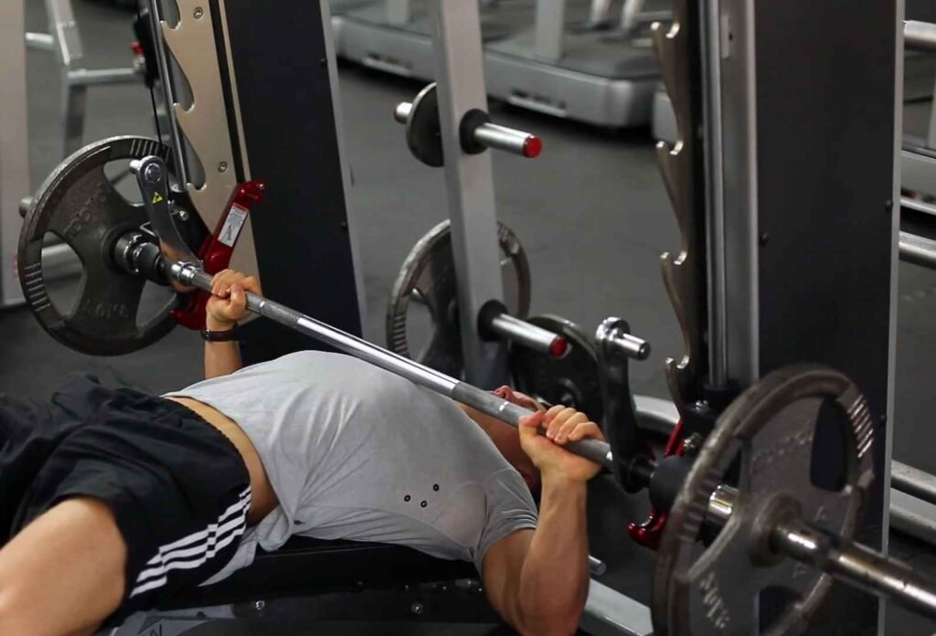 Pessoa realizando supino em máquina de academia com pesos ajustáveis.