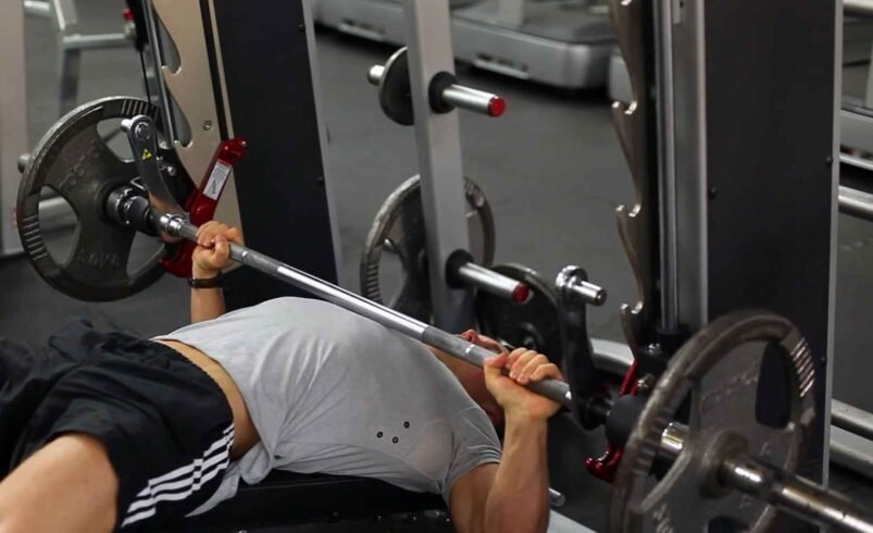 Pessoa realizando supino em máquina de academia com pesos ajustáveis.