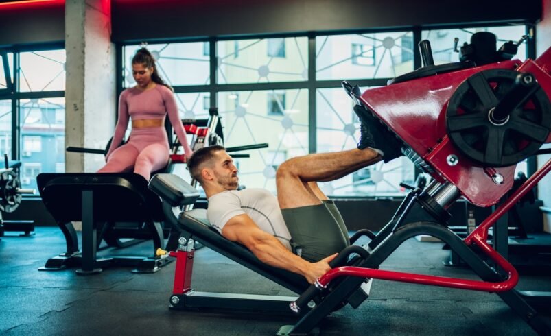 Homem usando máquina de leg press em academia moderna.