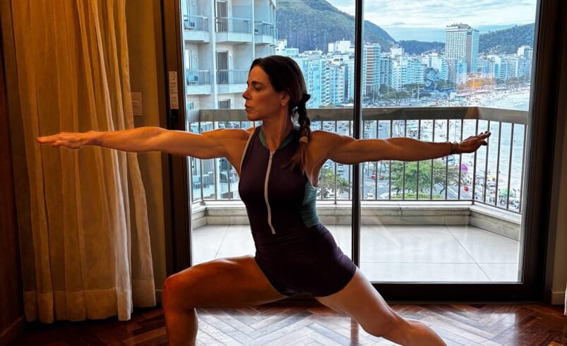 Prática de ioga em posição guerreiro em frente a uma sacada com vista urbana.