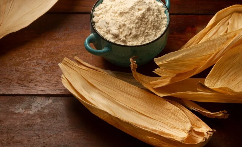 Vasilha azul com farinha de milho cercada por folhas secas.