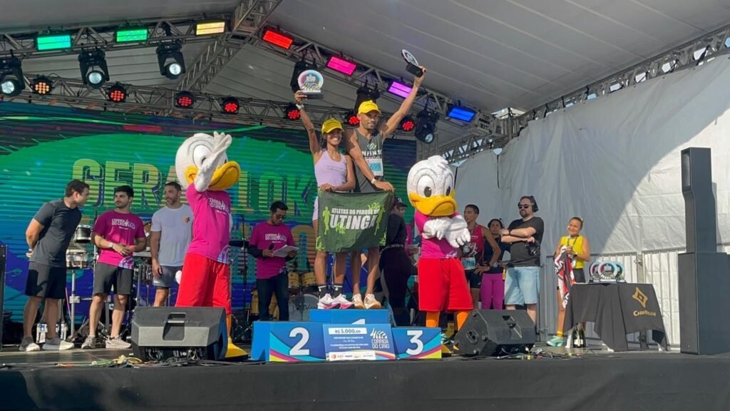 Pessoas comemorando em um pódio junto a mascotes em um evento ao ar livre.