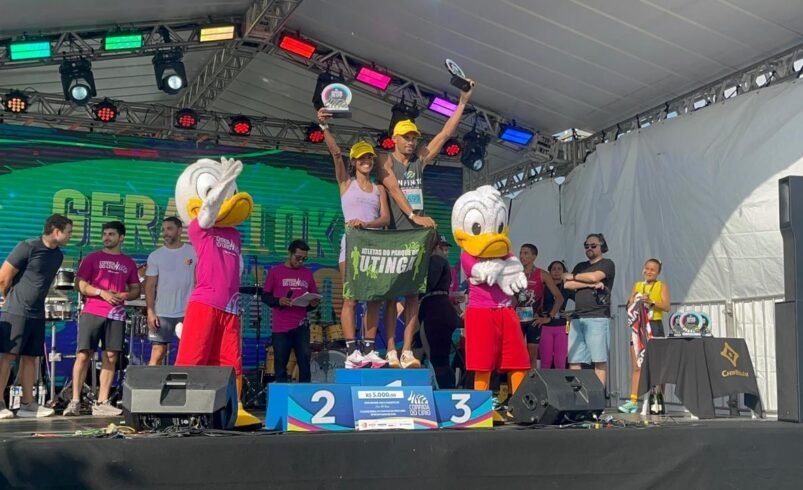 Pessoas comemorando em um pódio junto a mascotes em um evento ao ar livre.
